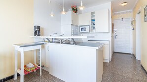 Une cuisine compacte avec des meubles blancs, un four à micro-ondes encastré, une machine à café et des luminaires suspendus.