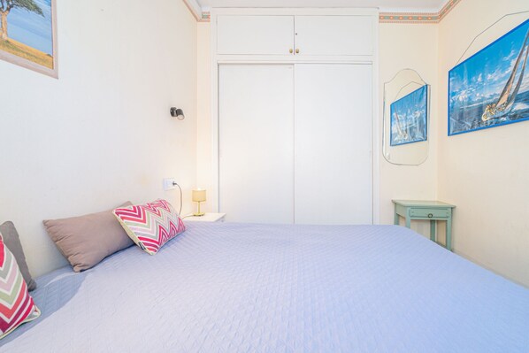 Un dormitorio con cama, almohadas, mesita de noche, lámpara, armario y decoración en la pared.