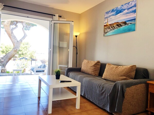 A living room with a grey sofa, a white coffee table, and a painting of a coastal scene. - DUPLEX SEMI-DETACHED HOUSE in complex with community pool, Air conditioning. (Puerto Addaya)