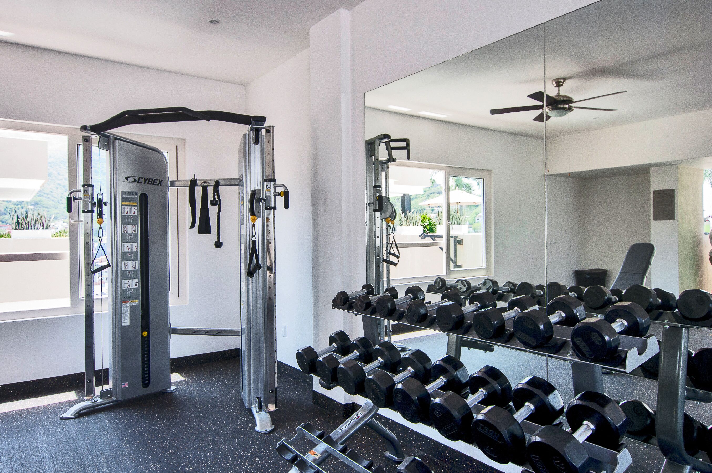 Un gimnasio con equipo de levantamiento de pesas, incluyendo una máquina Cybex y mancuernas.
