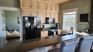 Een moderne keuken met een centraal eiland, houten kastjes, een roestvrijstalen koelkast en een groot raam voor natuurlijk licht.