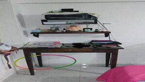 Een kamer met een houten bureau, een bed met een roze deken en een witte muur.