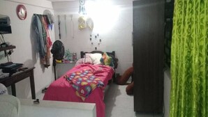 Een kleine, rommelige slaapkamer met een bed, een kledingkast, een ventilator en persoonlijke spullen.
