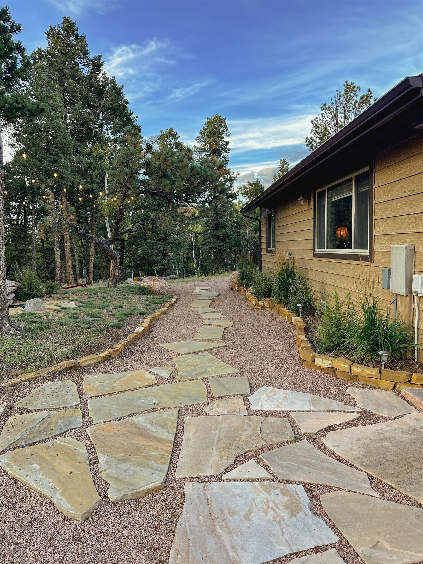 A stone pathway leading to a wooden house surrounded by trees.