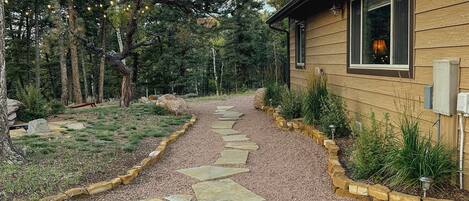 A stone pathway leading to a wooden house surrounded by trees.