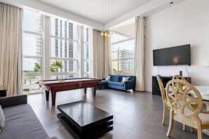 Un salon moderne avec une table de billard, un canapé, un téléviseur et une vue sur la ville.