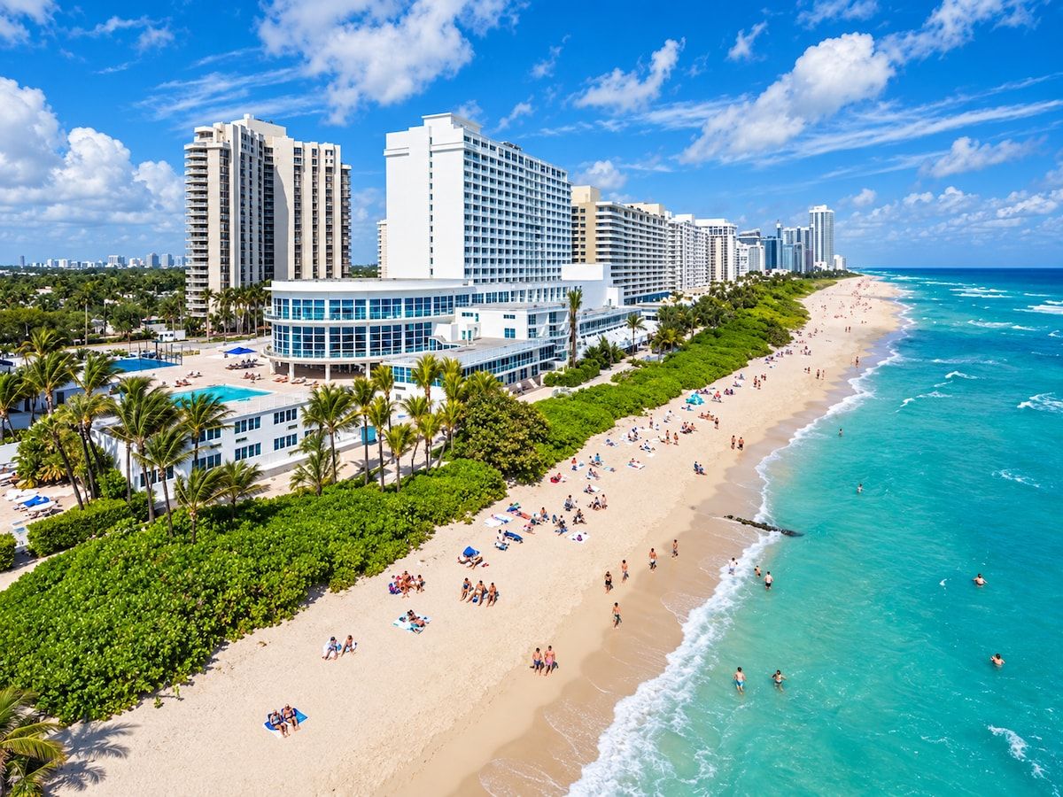 A coastal hotel with a beachfront, multiple high-rise buildings, and a sandy beach with people.