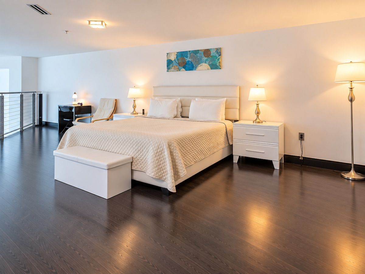 A modern hotel room with a large bed, bedside tables, a bench, and a painting on the wall.