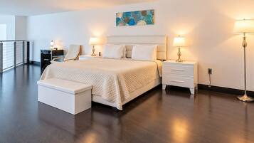 A modern hotel room with a large bed, bedside tables, a bench, and a painting on the wall.