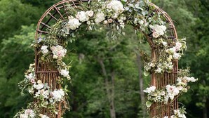 A rustic wooden arch adorned with white and pink flowers, set in a grassy outdoor area. - All inclusive Bed and Breakfast (McCloud)