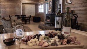 A wooden interior with a dining area, a fireplace, and a table with a cheese platter, wine glasses, and bottles. - All inclusive Bed and Breakfast (McCloud)