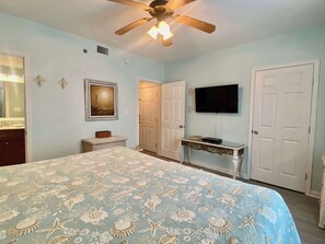 Une chambre à coucher avec un lit, un ventilateur de plafond, une télévision et une porte.