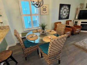 Un coin repas avec une table en verre, des chaises en osier et une horloge au mur.