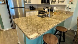 Una cocina con encimeras de granito, electrodomésticos de acero inoxidable, armarios blancos y salpicadero verde azulado.