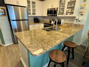 A kitchen with granite countertops, stainless steel appliances, white cabinets, and a teal backsplash. - Tropic Isles 101 (Gulf Shores)