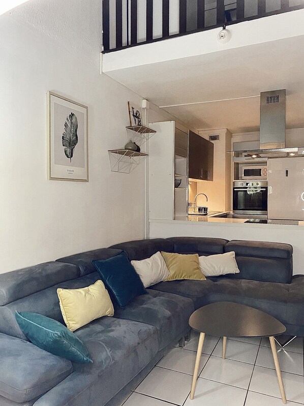 A modern living room with a sectional sofa, a small round table, and a kitchen in the background.