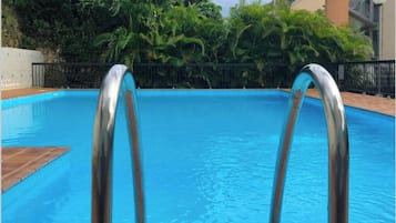 A swimming pool with metal ladders, surrounded by lush greenery and a building in the background.