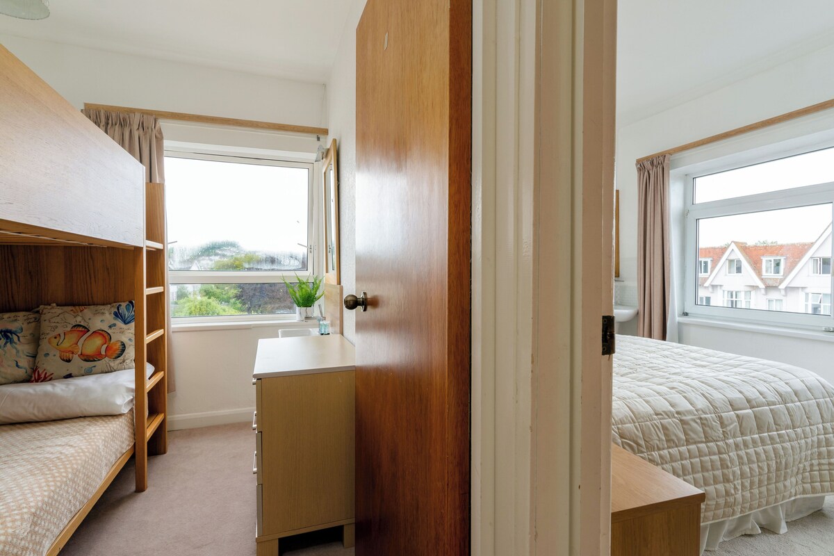 A bedroom with bunk beds, a desk, and a window with a view of houses.