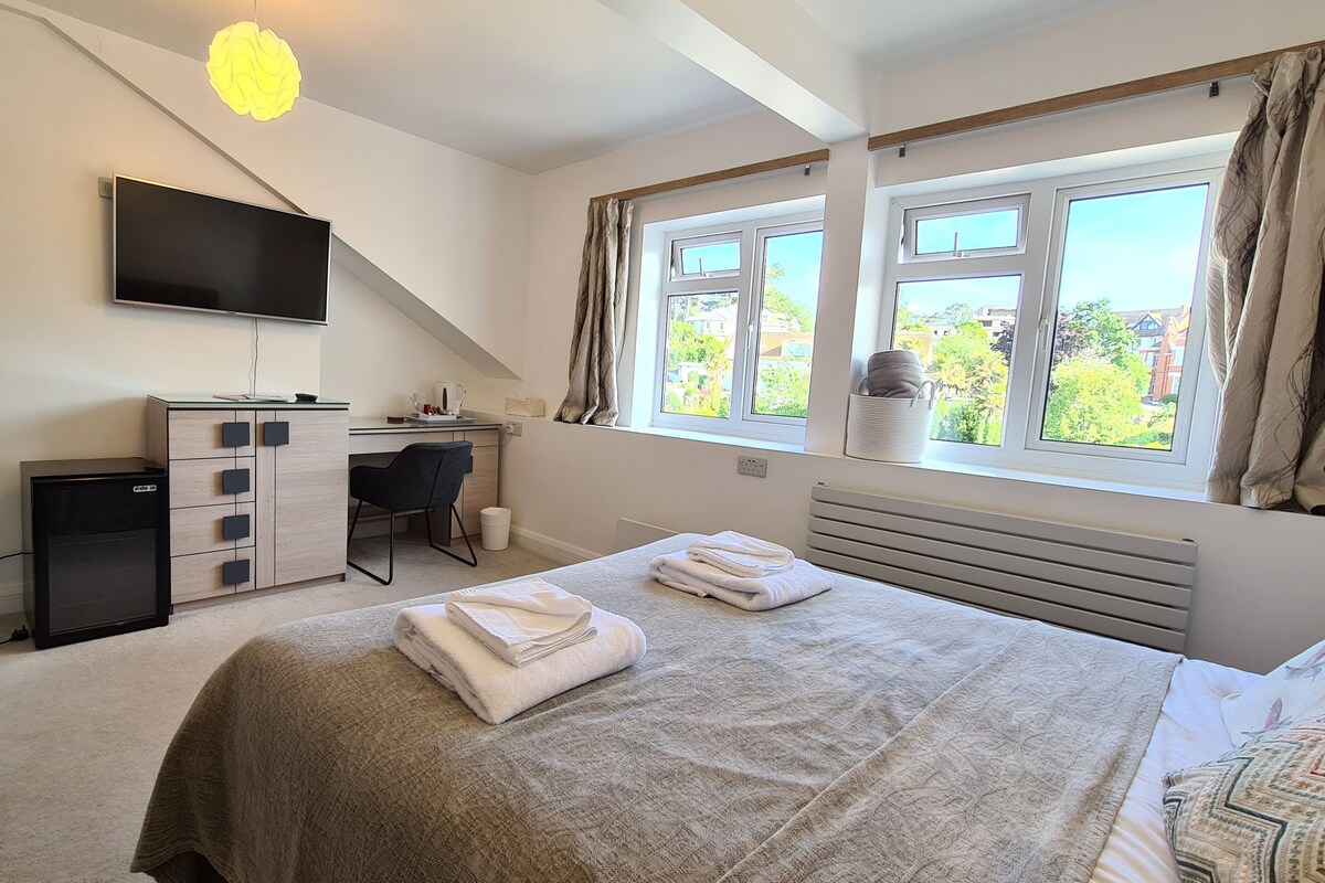 A bedroom with a bed, a desk, a TV, and a window with curtains.