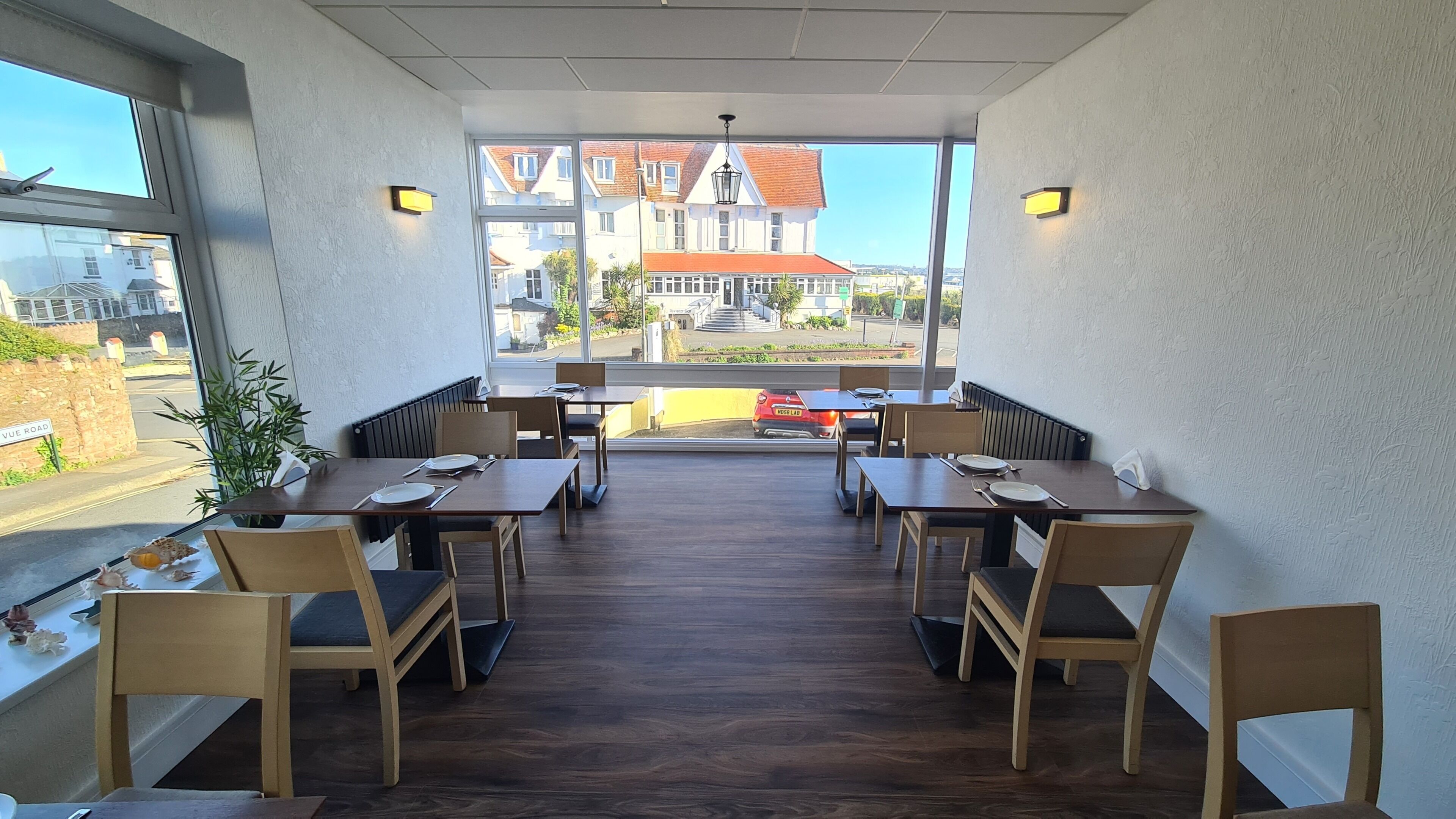 A restaurant with wooden tables and chairs, a view of buildings outside, and a street sign visible through the window.