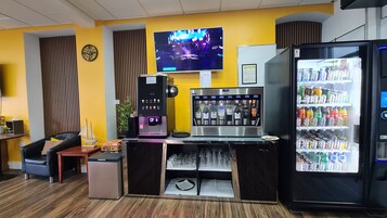 Zona de bar con pantalla de televisión, dispensador de bebidas y nevera llena de refrescos.