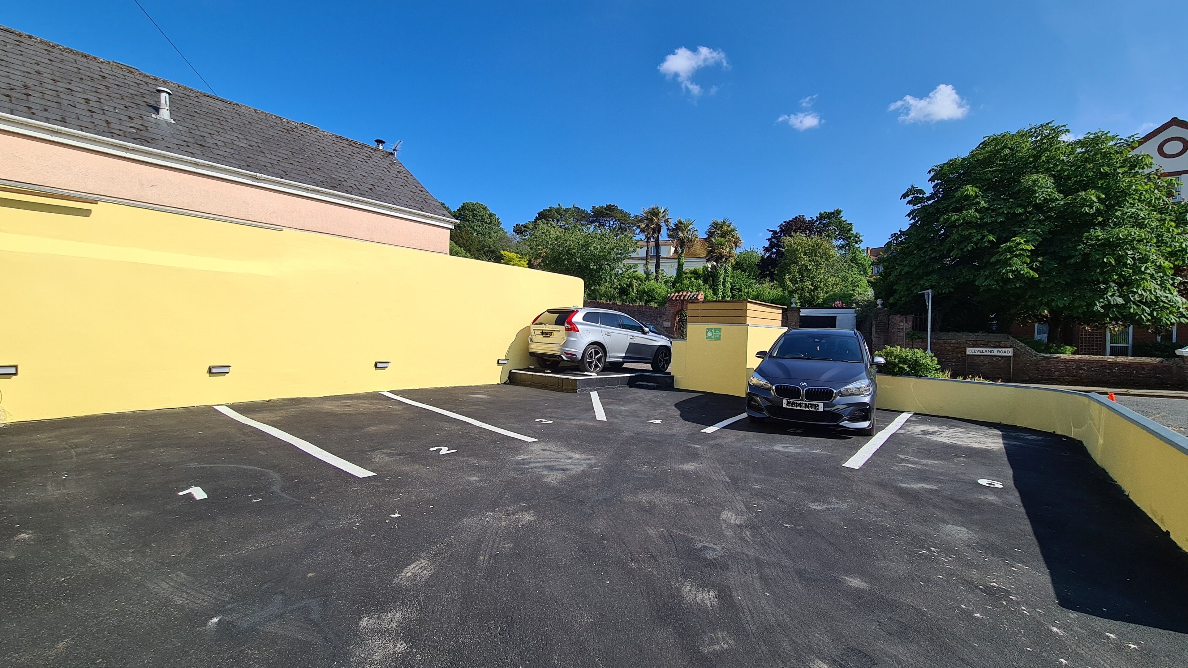 Un parking avec deux voitures, un mur jaune et un panneau indiquant la direction de Cleveland Road.
