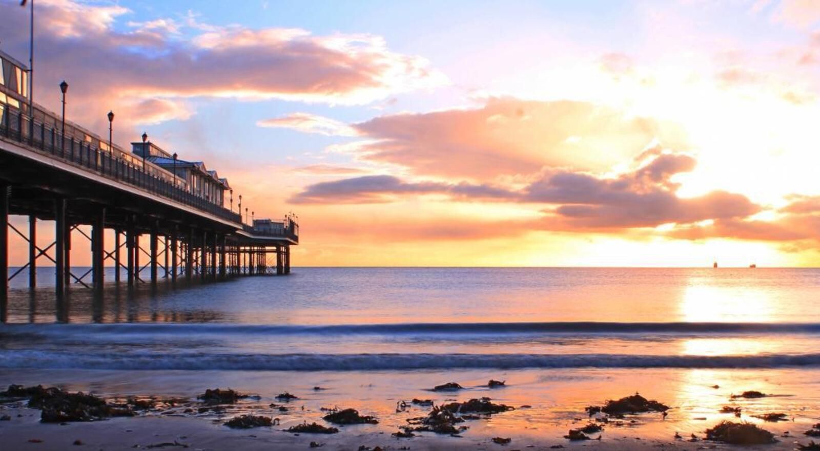 A pier extending into the sea with a sunset in the background.