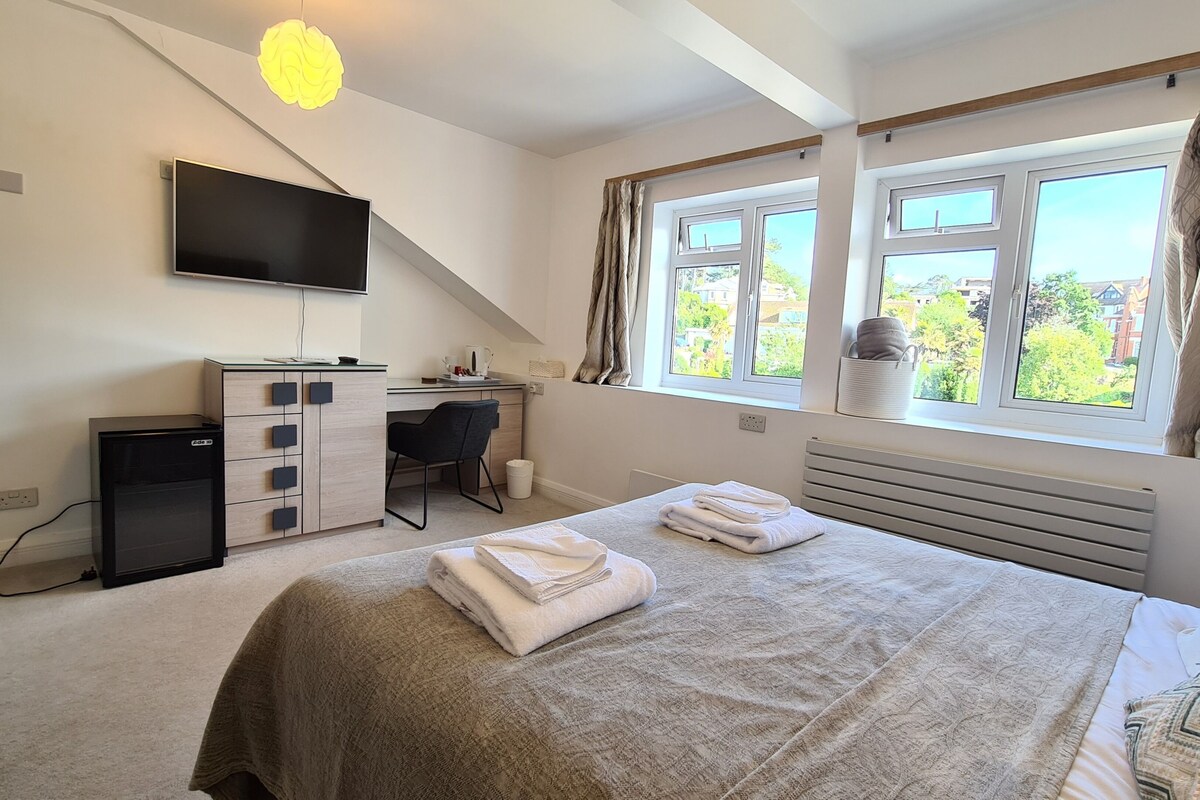 A bedroom with a bed, a desk, a TV, and a window with curtains.