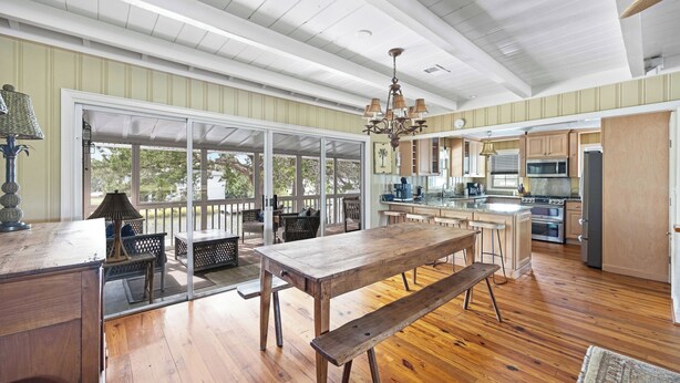 A spacious kitchen with wooden flooring, a large dining table, and a view through a glass door to an outdoor patio. - Beach House on Tidal Creek, Dock, Screen Porch, Easy Walk to Beach, Dog Friendly (Pawleys Island)