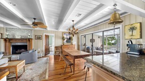 A spacious living area with a fireplace, wooden flooring, a large dining table, and a view to the outdoors. - Beach House on Tidal Creek, Dock, Screen Porch, Easy Walk to Beach, Dog Friendly (Pawleys Island)