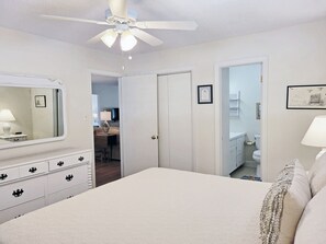 A bedroom with a bed, dresser, ceiling fan, and a door leading to a bathroom.
