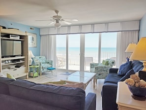 A living room with a television, sofa, chairs, a coffee table, and a view of the ocean.