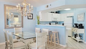 A modern kitchen with white cabinets, a glass dining table, and a chandelier. - Oceanfront Condo, Top Floor Ocean View, Elevator, Pool, Hot Tub, Beach Access (Pawleys Island)