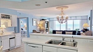 A modern kitchen with a central island, a dining area with chairs, a chandelier, and a view of the ocean. - Oceanfront Condo, Top Floor Ocean View, Elevator, Pool, Hot Tub, Beach Access (Pawleys Island)