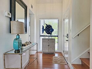 Stylish hallway with a glass door, console table, and teal lamp, leading to a staircase.
