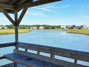 A wooden deck with a bench overlooking a calm body of water, surrounded by houses and greenery. - Second Row Condo, Covered Parking, Creek Dock, 2 Pools, Access to 7-Mile Beach (Pawleys Island)