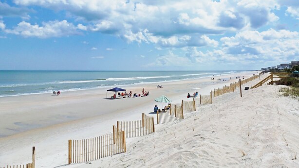 A beach with a wooden fence, umbrellas, and people relaxing.