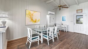 Ein Essbereich mit einem Glastisch und weißen Stühlen, einem Deckenventilator und einem großen abstrakten Gemälde an der Wand.