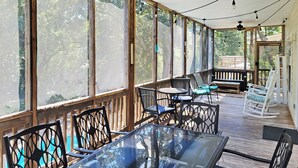 A covered outdoor area with a glass table and chairs, wooden deck, and large windows. - Private Pool Beach House, Dog Friendly, Easy Walk to Beach, Bike Path Nearby (Pawleys Island)