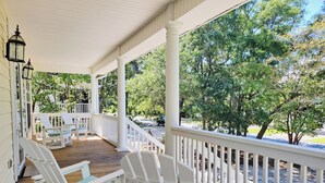 A covered porch with white railings and rocking chairs, overlooking a driveway and trees. - Private Pool Beach House, Dog Friendly, Easy Walk to Beach, Bike Path Nearby (Pawleys Island)