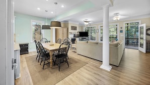 A spacious living room with a large sofa, a dining area with a wooden table and chairs, and a kitchen area with a TV and cabinets. - Private Pool Beach House, Dog Friendly, Easy Walk to Beach, Bike Path Nearby (Pawleys Island)