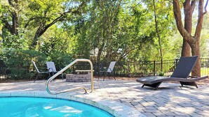 A swimming pool with a stone edge, surrounded by a paved deck, lounge chairs, and a stone bench. - Private Pool Beach House, Dog Friendly, Easy Walk to Beach, Bike Path Nearby (Pawleys Island)