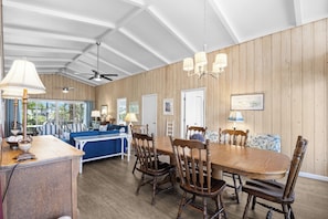 Un espace repas avec une table et des chaises en bois, un ventilateur de plafond et une vue dégagée grâce à de grandes fenêtres.