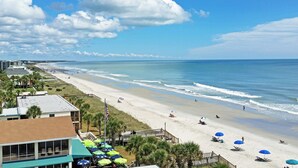 A beach with umbrellas, a flag, and a building with a green roof. - Canal Front Beach House, Screened Porch, 2 TV Dens, Dock, Short Block from Beach (Pawleys Island)