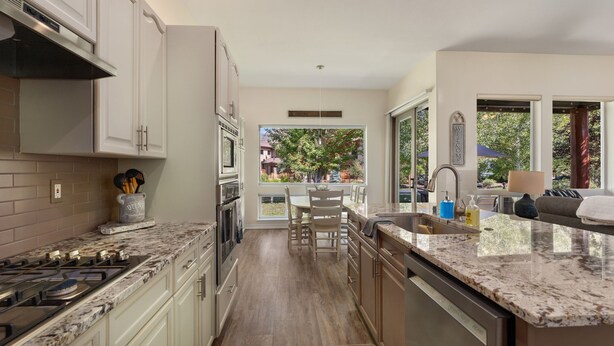 Cocina moderna con armarios blancos, encimera de granito y vistas a un jardín trasero a través de amplios ventanales.