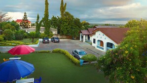Un quartier résidentiel avec une maison dotée d’un toit en tuiles, d’une allée pavée et d’un petit jardin agrémenté d’un parasol rouge et bleu.
