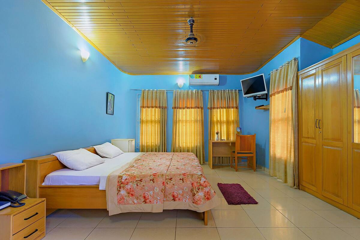 A bedroom with a bed, a desk, a wardrobe, a television, and a ceiling fan.