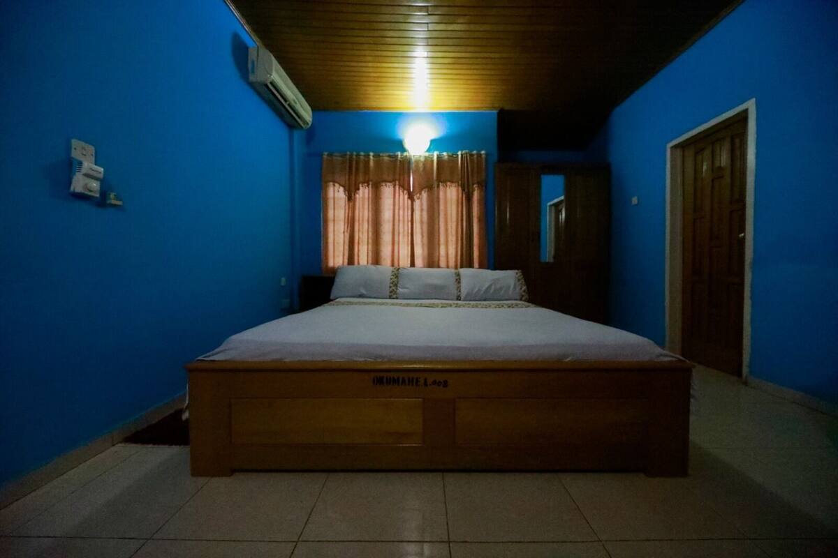 A bedroom with a wooden bed, blue walls, a ceiling fan, and a window with curtains.