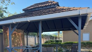 Eine überdachte Terrasse mit einer Pergola, Sitzgelegenheiten im Freien und Blick auf den Garten.