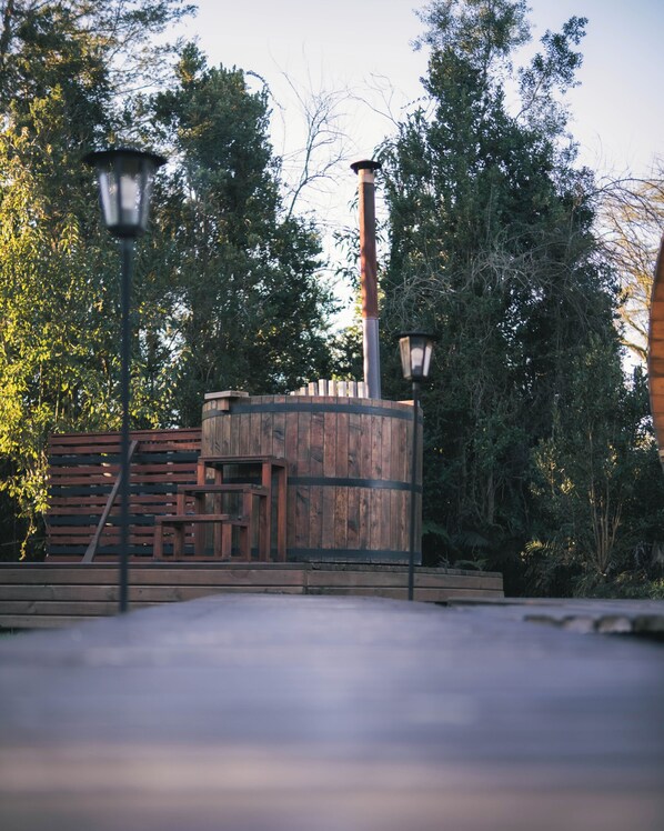 A rustic wooden structure with a chimney, surrounded by trees and a paved area.
